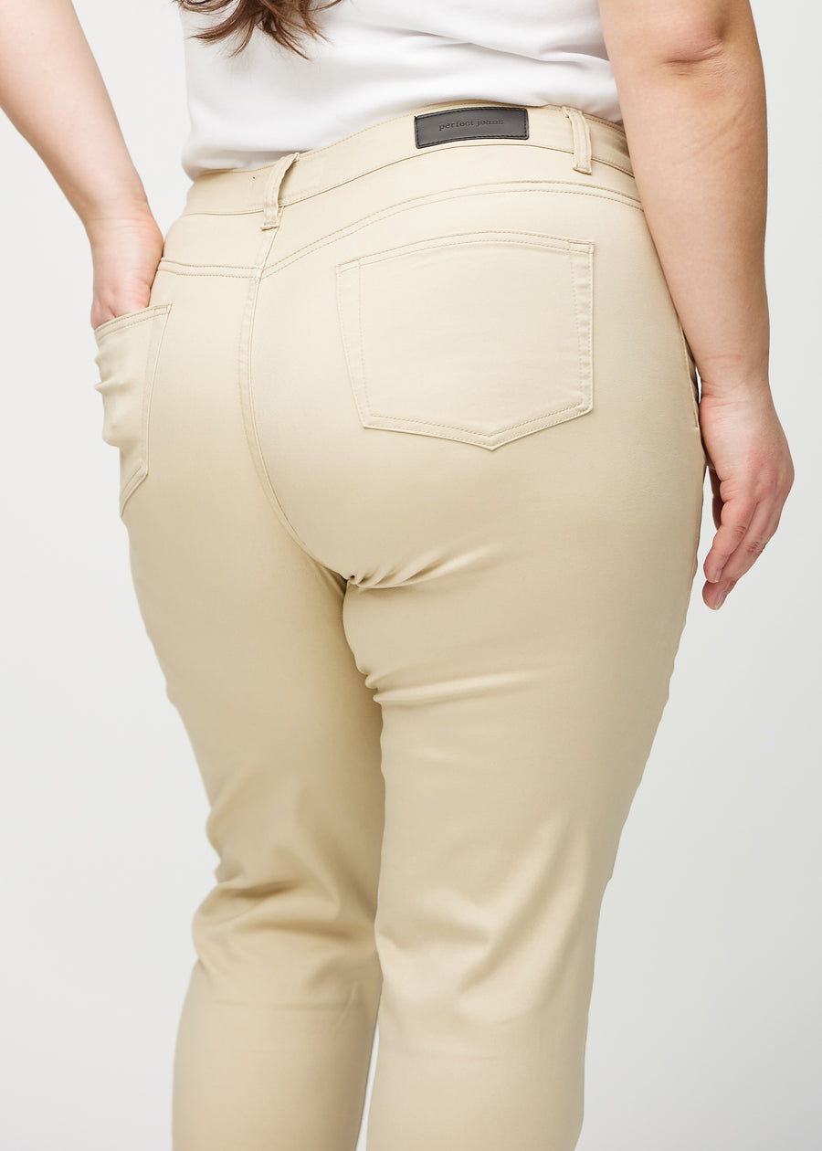 Beige slim jeans set bagfra tæt på en plus-size model for at vise detaljer.