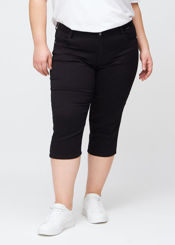 Sorte slim capris, farve Ravens, med tætsiddende pasform og længde lige under knæet – set forfra på plus-size model.