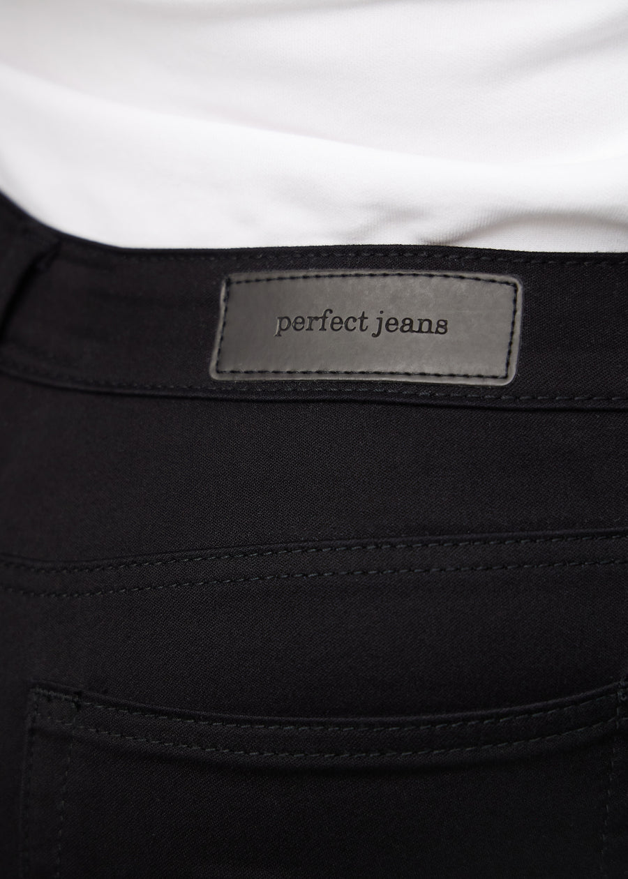 Close-up of black jeans material with the Perfect Jeans leather patch at the back of the waistband on a plus-size model.