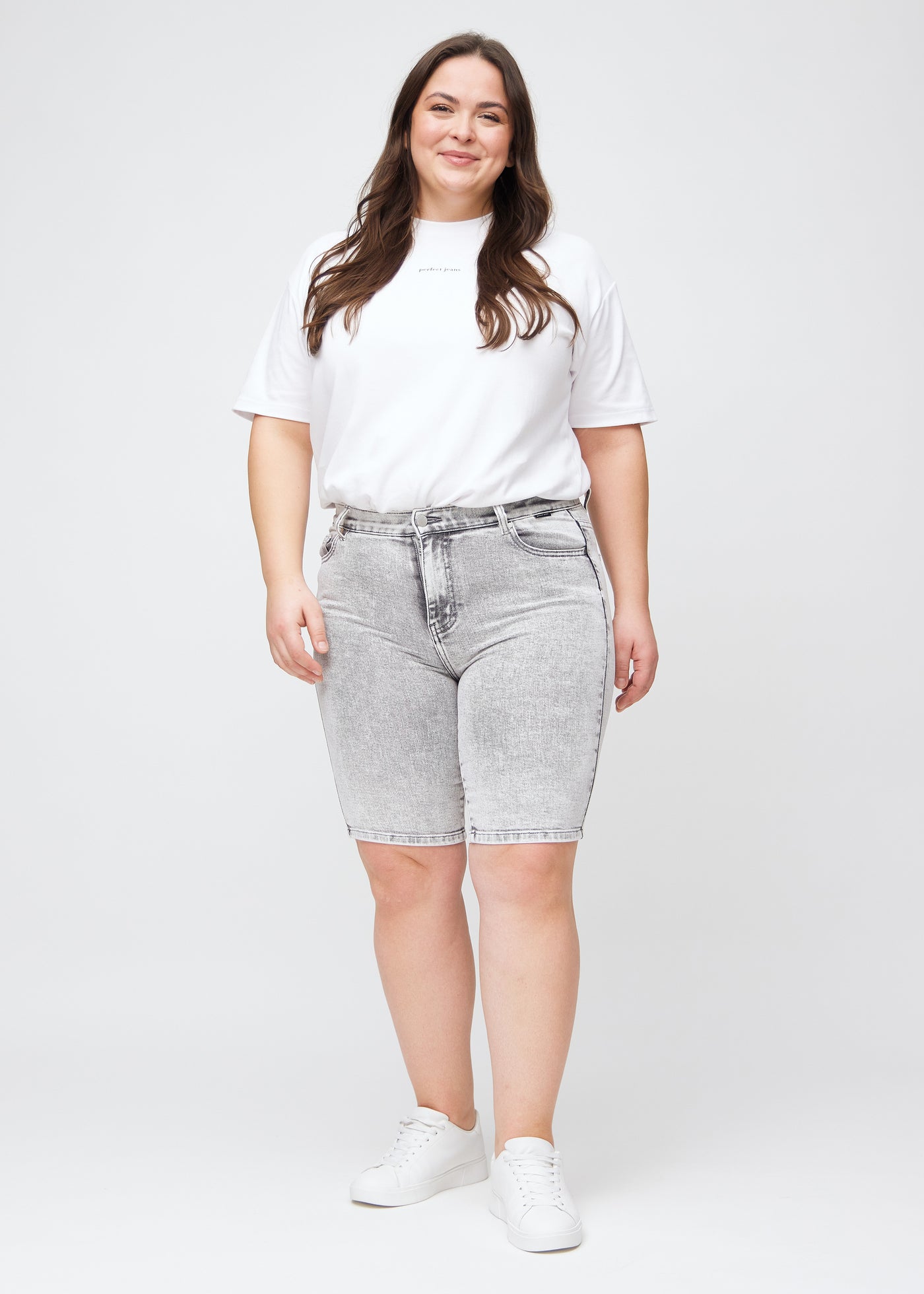 Fuldt billede af en plus-size model i lysegrå denim skinny middle shorts.