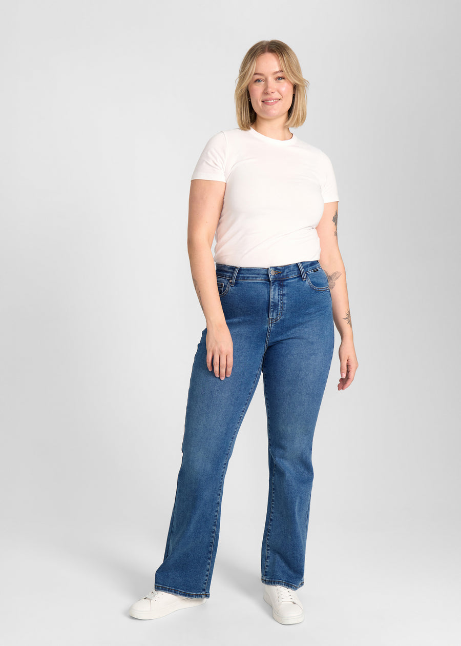 Fuldt billede af model i mørkeblå denim bootcut jeans på en plus-size model.