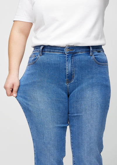 Plus-size model strækker jeansene ved låret for at vise stretch.
