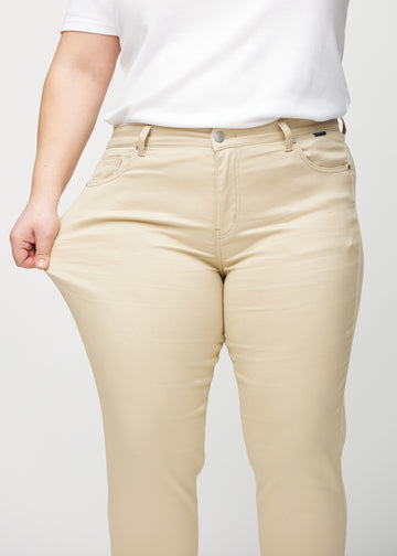 Plus-size model strækker jeansene ved låret for at vise stretch.