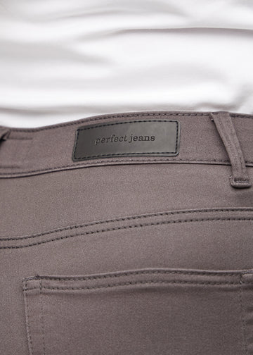 Nærbillede af gråbrunt jeansmateriale med Perfect Jeans læderpatch bagpå i taljen, på en plus-size model.