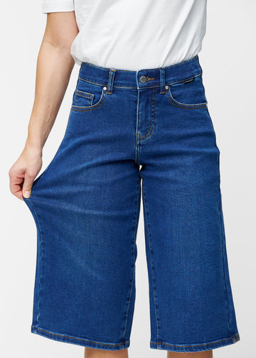 Model strækker de løse, mørkeblå denim capris i farven Oceans ved hoften for at vise materialets stretch.