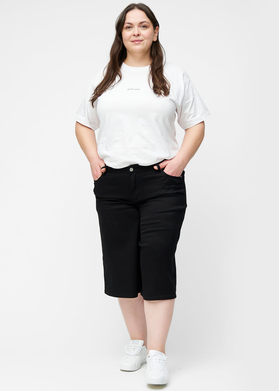 Fuldt billede af plus-size model i løse, sorte capris i farven Ravens, der går til lige under knæet.