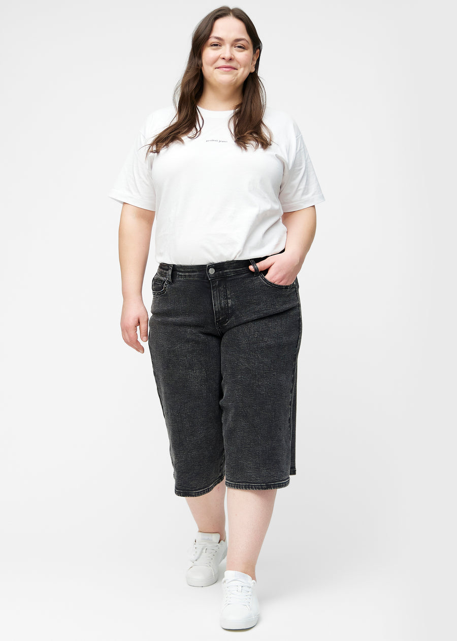 Fuldt billede af plus-size model i løse, mørkegrå denim capris i farven Shadows, der går til lige under knæet.