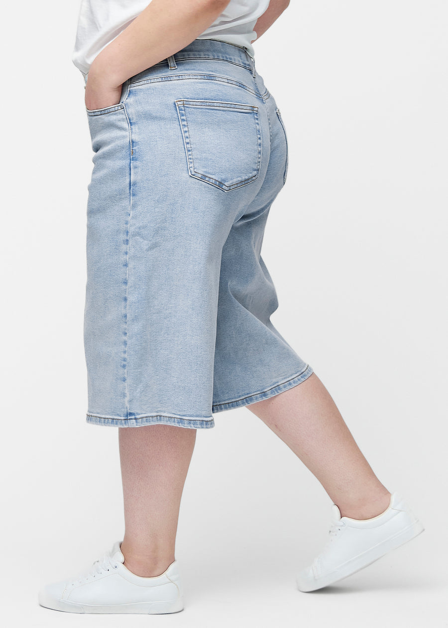 Loose, light blue denim capris in the colour Waves seen from the side on a plus-size model, where the wide fit and length to just below the knee are visible.