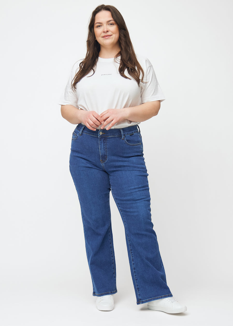 Dark blue mid-rise bootcut jeans in Oceans. Full-length view of a plus-size model wearing the jeans.