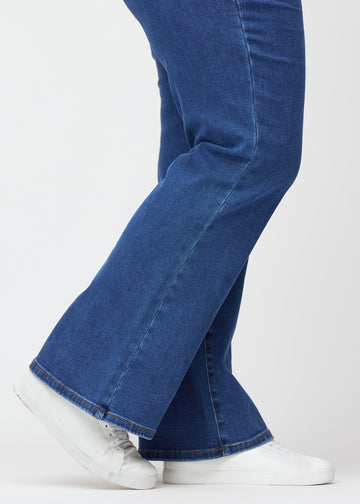Dark blue mid-rise bootcut jeans in Oceans. Close-up of the ankle area on a plus-size model, showing the subtle bootcut flare.