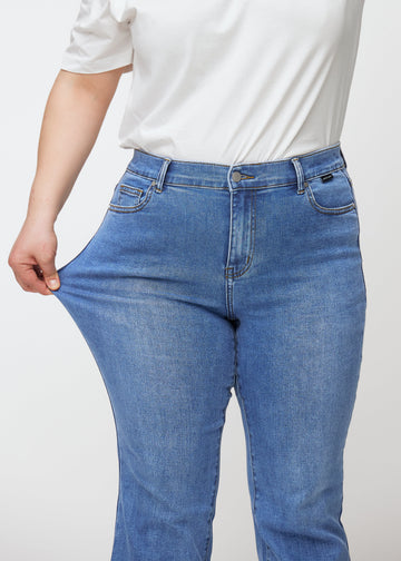 Blue mid-rise bootcut jeans in Rivers. A plus-size model stretches the jeans at the thigh to show the fabric&