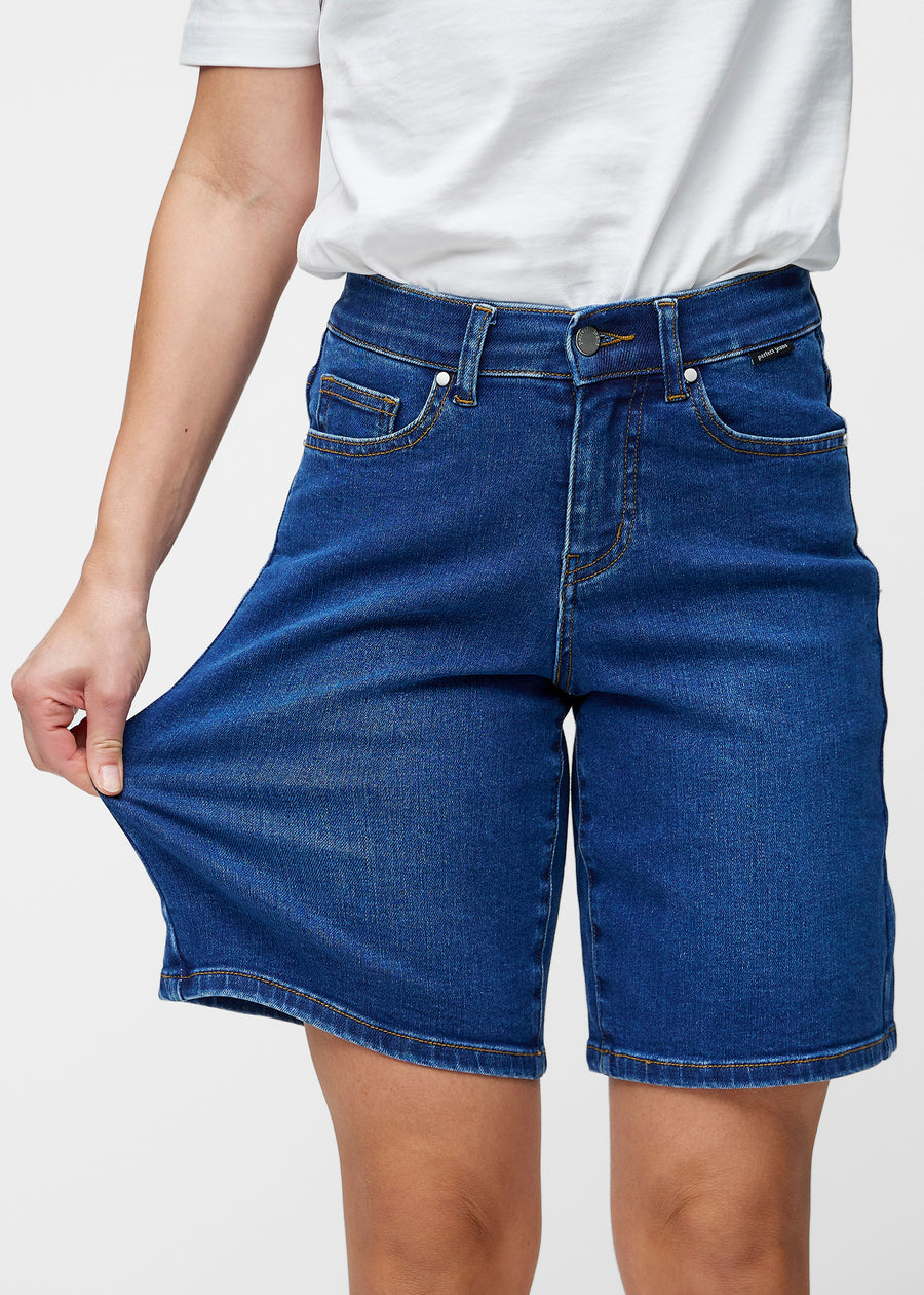 Model strækker de løse, mørkeblå denim shorts i farven Oceans ved hoften for at vise materialets stretch.