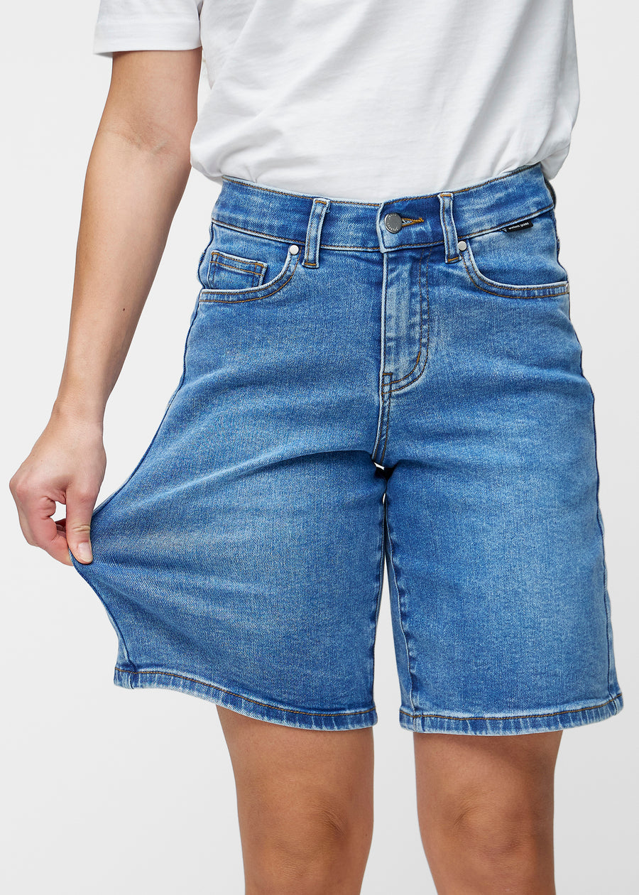 Model strækker de løse, klassisk blå denim shorts i farven Rivers ved hoften for at vise materialets stretch.
