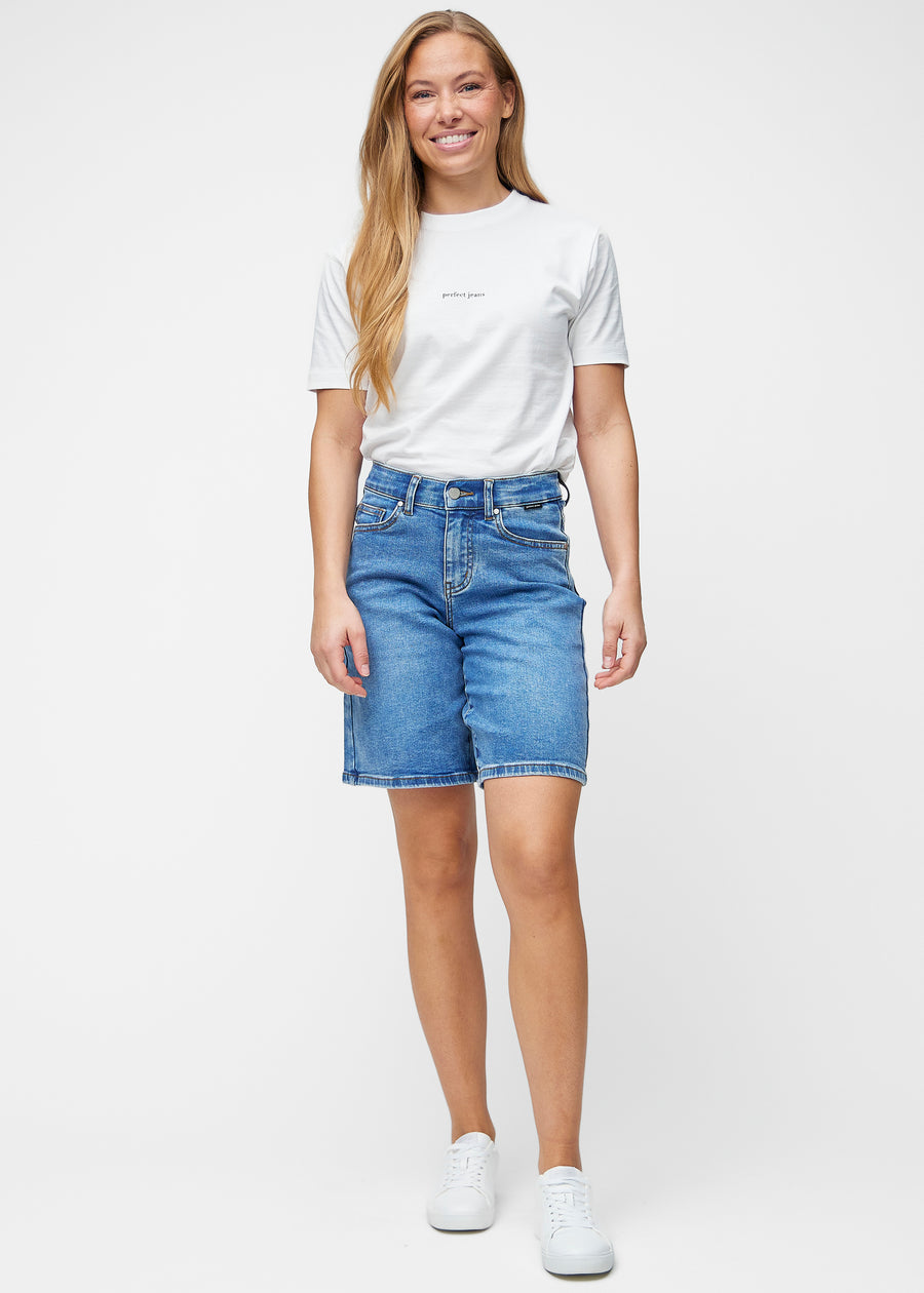 Fuldt billede af model i løse, klassisk blå denim shorts i farven Rivers, der går til lige over knæet.