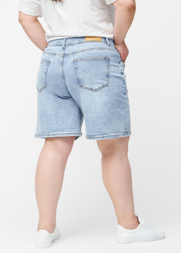 Loose, light blue denim shorts in the colour Waves seen from the side on a plus-size model, where the wide fit and length to just above the knee are visible.