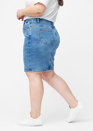 Klassisk blå, tætsiddende og knælang denimnederdel set fra siden på plus-size model.
