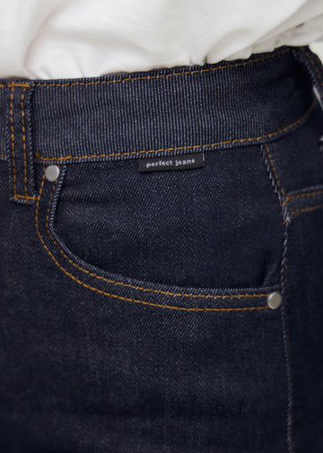 Close-up of deep dark blue denim with Perfect Jeans logo label at the front pocket edge.