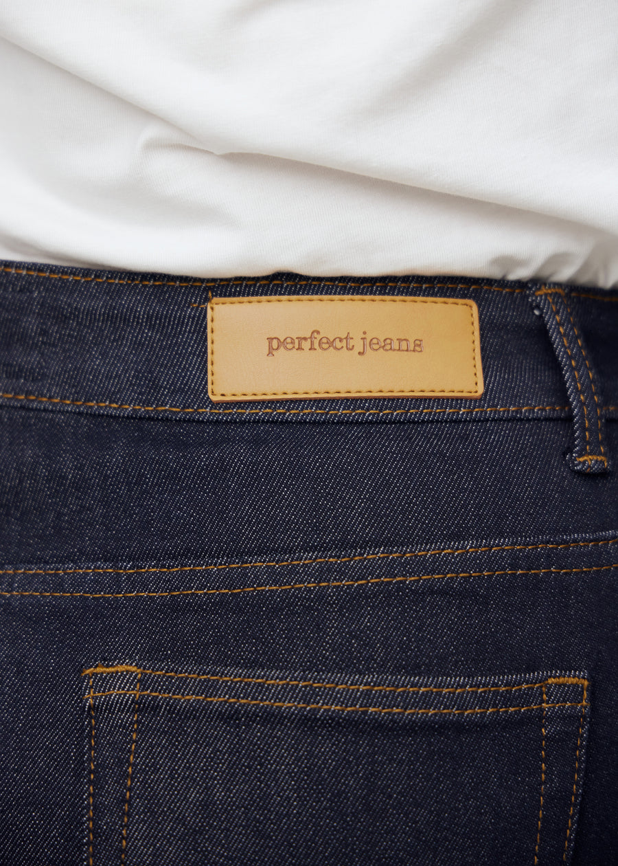Close-up of deep dark blue denim with Perfect Jeans leather patch at the back waist on a plus-size model.