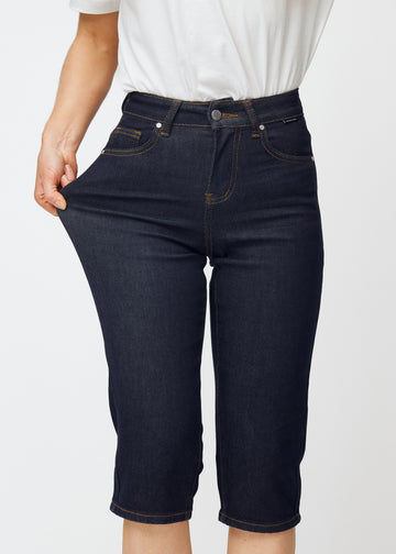 Model stretches deep dark blue denim capris for women in the colour Midnights at the thigh to show the material’s stretch.