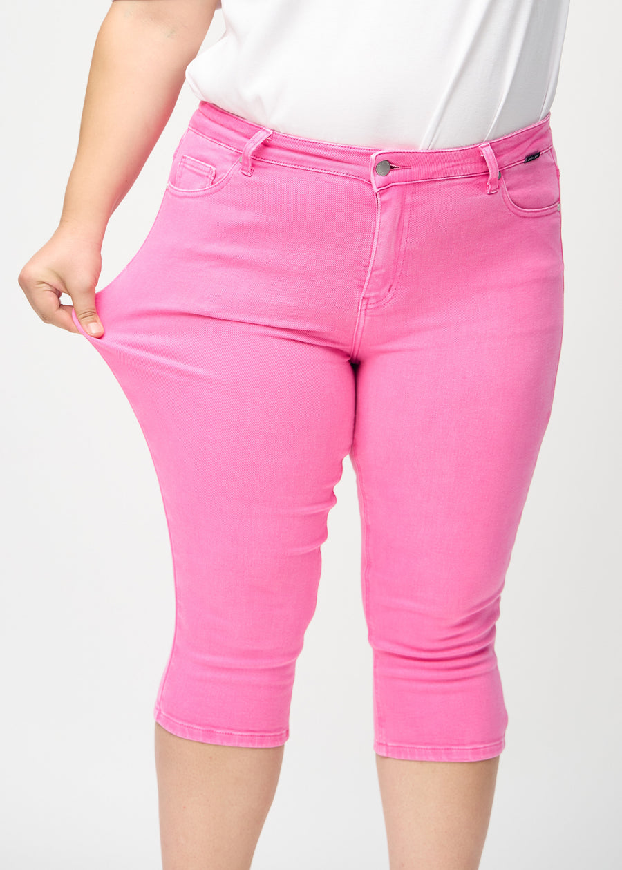 Skinny capris for women in pastel pink fabric, color Flamingos. A plus-size model stretches the fabric to demonstrate its flexibility.