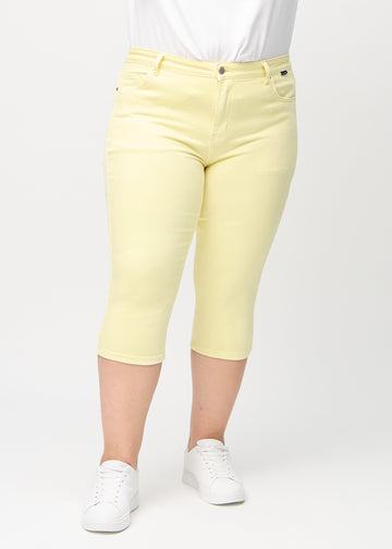 Skinny capris for women in pastel yellow fabric, color Lemonades. Front view on a plus-size model, showing the close-fitting legs ending just below the knee.