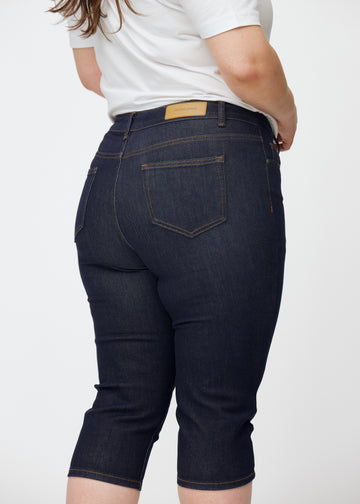 Deep dark blue denim capris for women in the colour Midnights seen from the back in close-up on a plus-size model.