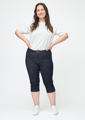 Full image of a plus-size model wearing deep dark blue denim capris for women in the colour Midnights with a skinny fit.
