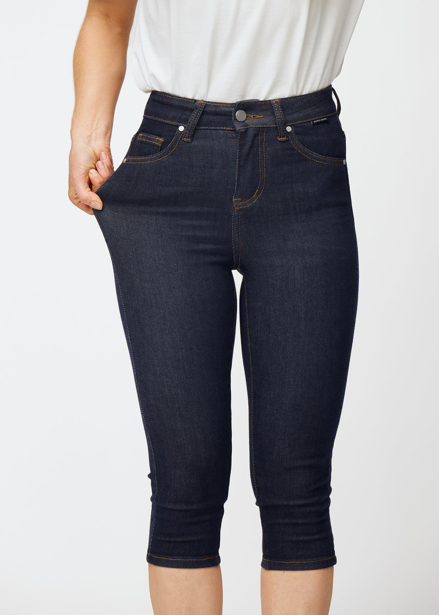 Model stretches deep dark blue denim capris for women in the colour Midnights at the thigh to show the material’s stretch.