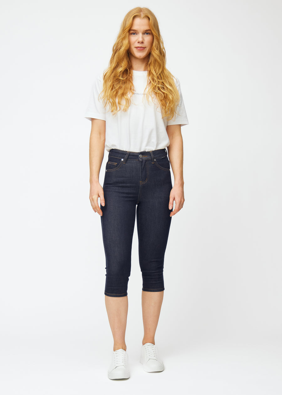 Full image of a model wearing deep dark blue denim capris for women in the colour Midnights with a skinny fit.