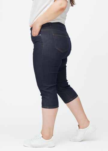 Deep dark blue denim capris for women in the colour Midnights with a skinny fit seen from the side on a plus-size model.