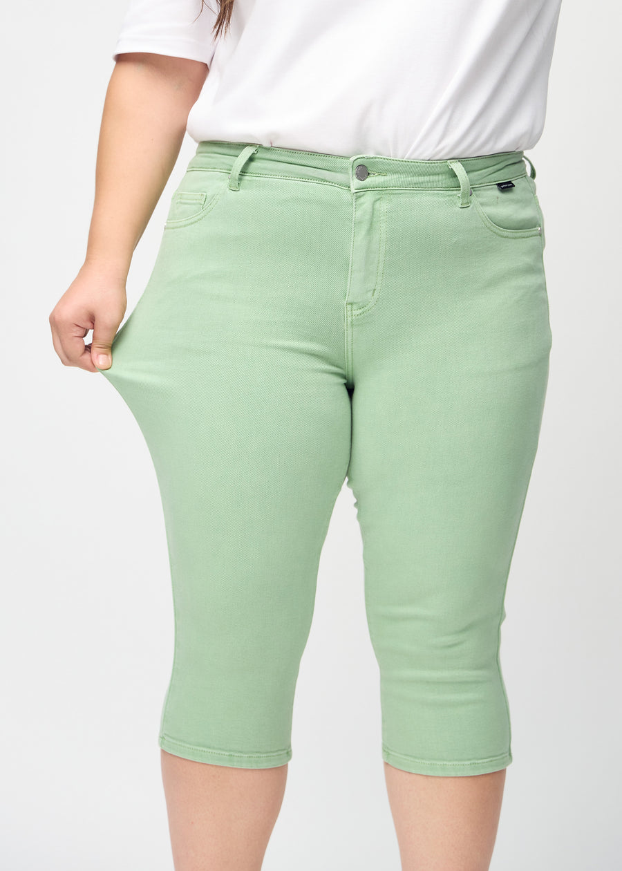 Skinny capris for women in pastel green fabric, color Mints. A plus-size model stretches the fabric to demonstrate its flexibility.