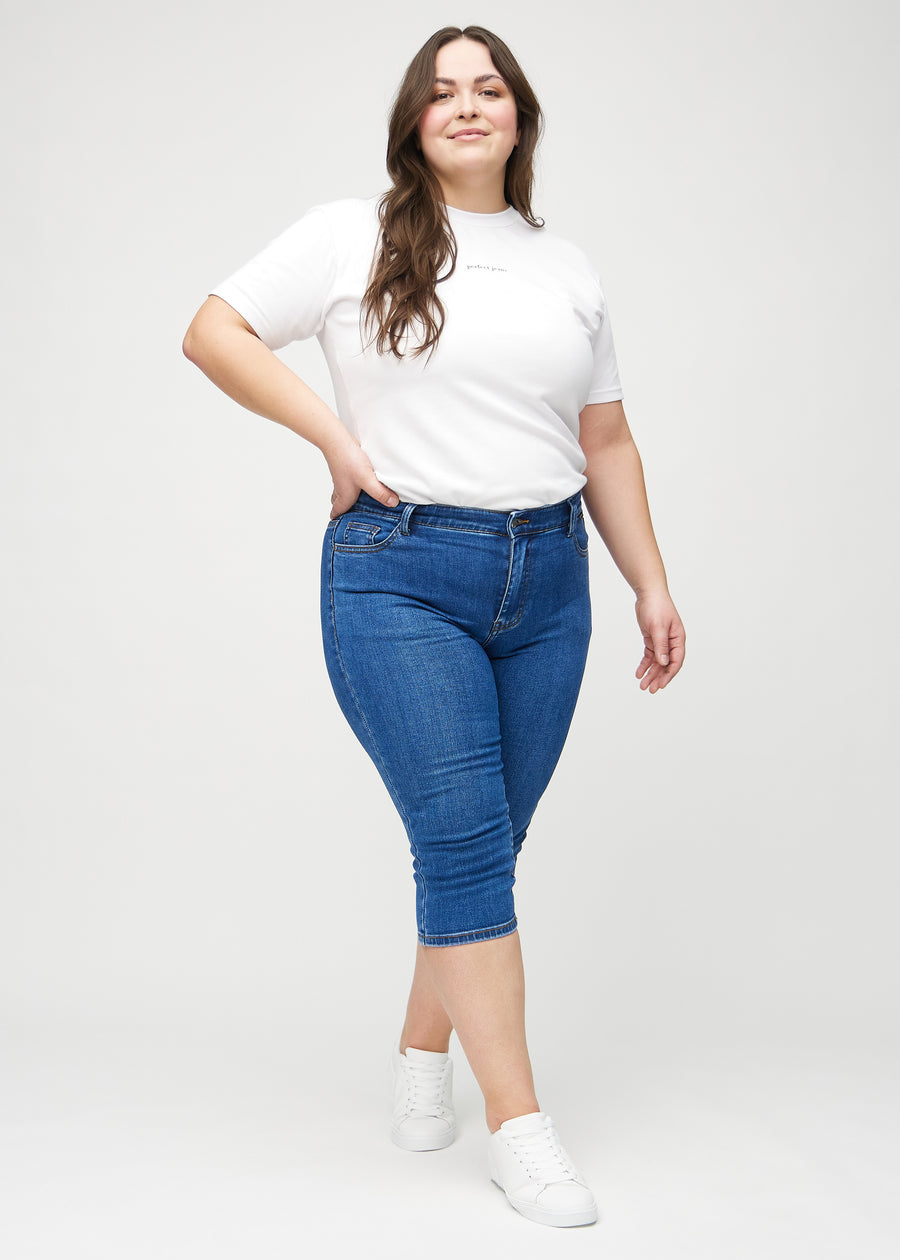 Skinny capris for women in dark blue denim, color Oceans. Full-length view of a plus-size model wearing the capris.