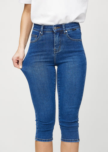 Skinny capris for women in dark blue denim, color Oceans. A model stretches the fabric to demonstrate its flexibility.