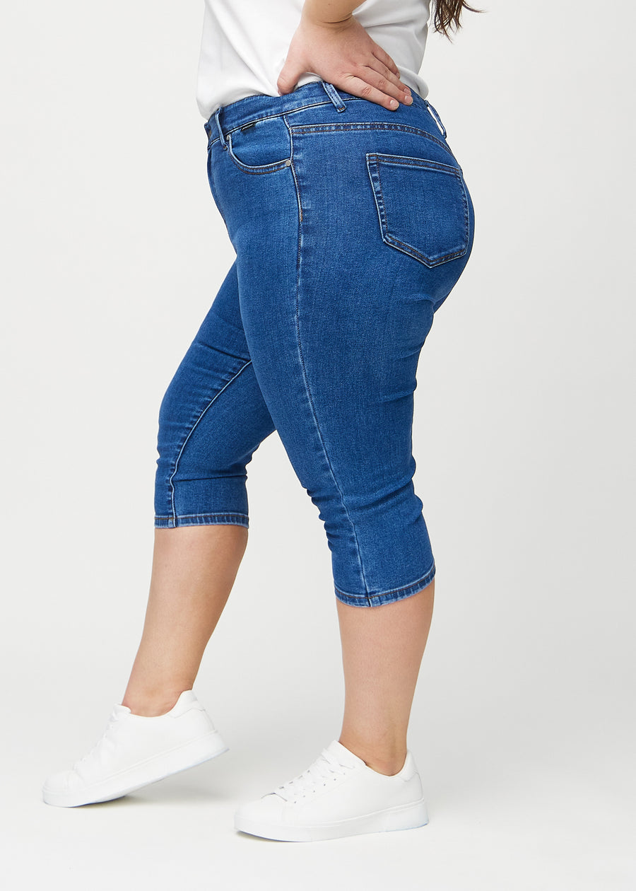 Skinny capris for women in dark blue denim, color Oceans. Side view on a plus-size model, showing the fitted cut.