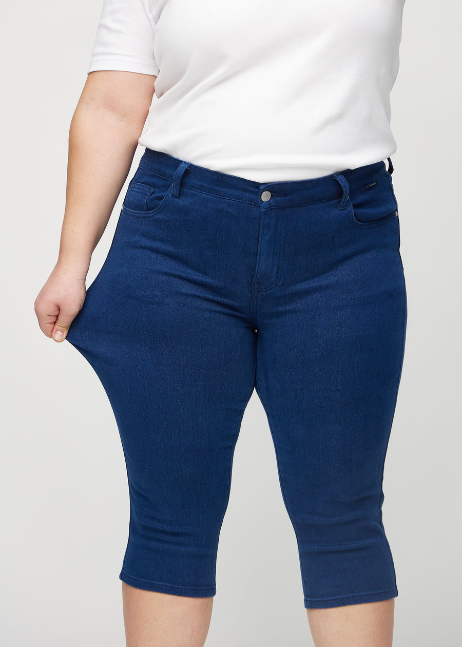 Skinny capris for women in dark blue fabric, color Royals. A plus-size model stretches the fabric to demonstrate its flexibility.