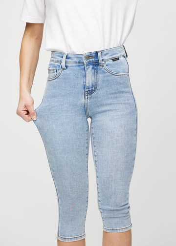 Skinny capris for women in light blue denim, color Waves. A model stretches the fabric to demonstrate its flexibility.