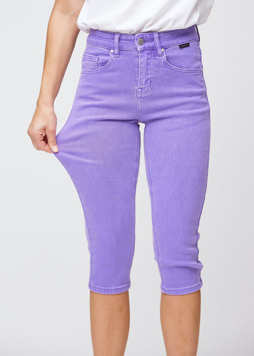 Slim capris for women in pastel purple jeans fabric, color Lavenders. A model pulls the fabric at the thigh to demonstrate stretch and flexibility.