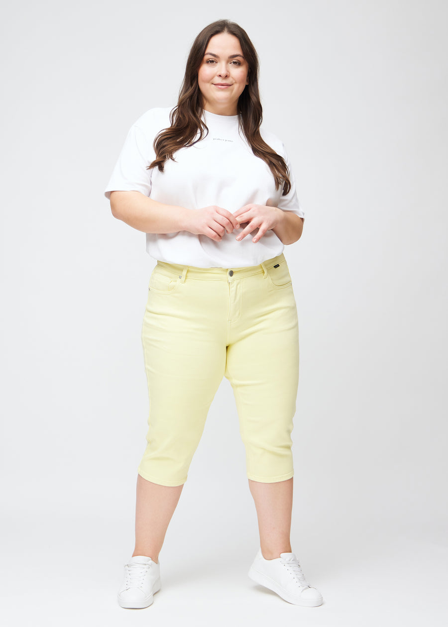 Slim capris for women in pastel light yellow jeans fabric, color Lemonades. Full-length view of a plus-size model wearing slim capris.