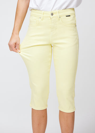 Slim capris for women in pastel light yellow jeans fabric, color Lemonades. A model pulls the fabric at the thigh to demonstrate stretch and flexibility.