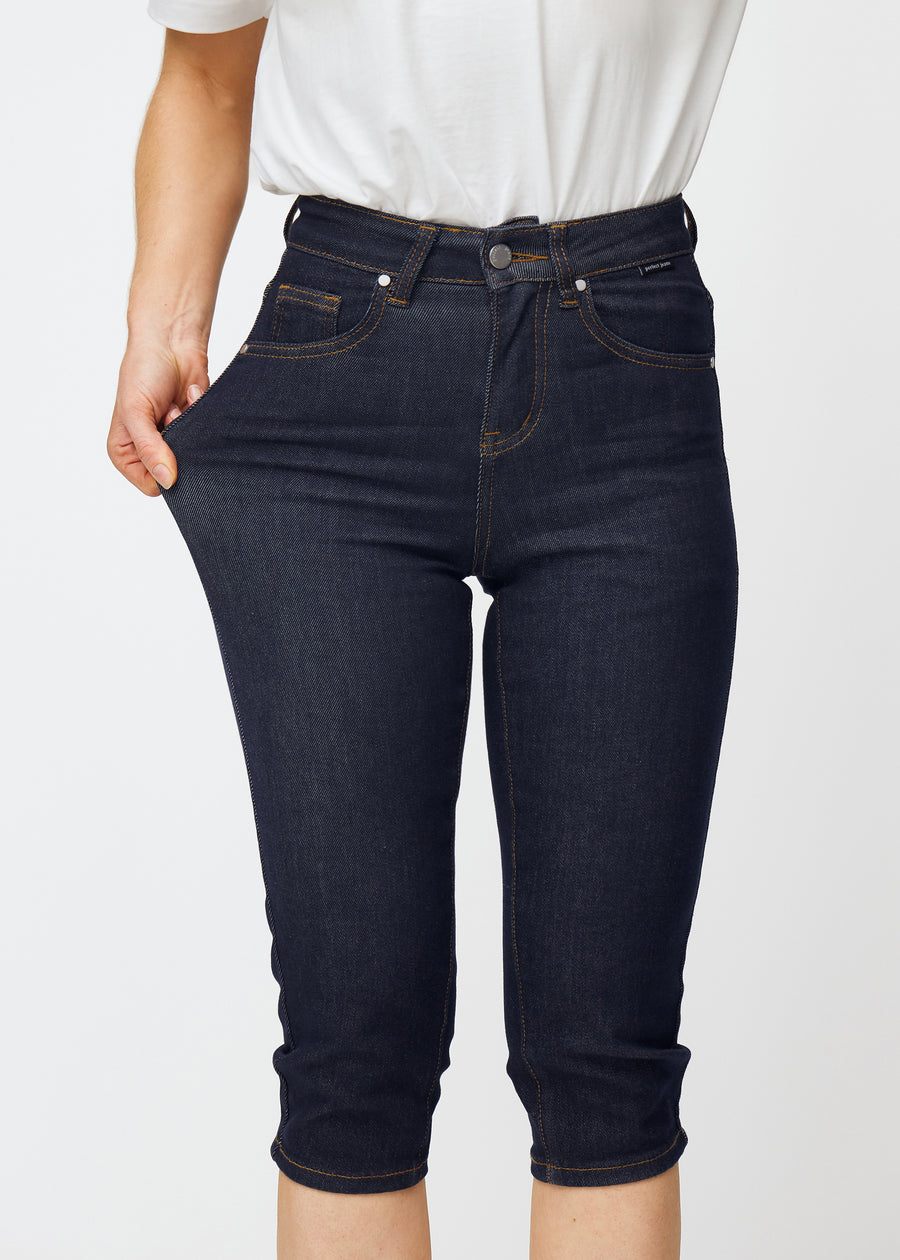 Model stretches deep dark blue denim capris for women in the colour Midnights at the thigh to show the material’s stretch.