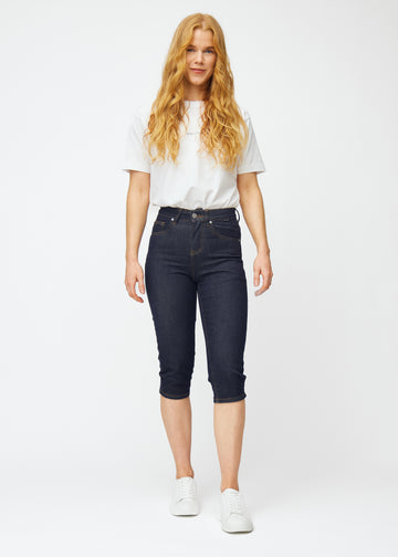 Full image of a model wearing deep dark blue denim capris for women in the colour Midnights with a slim fit.