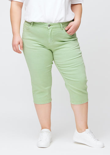 Slim capris for women in pastel light green jeans fabric, color Mints. Front view on a plus-size model, showing the fitted cut ending just below the knee.