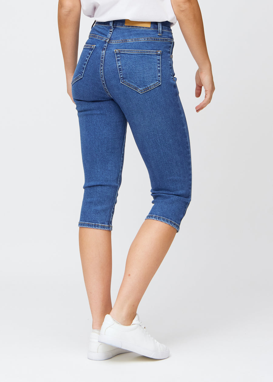 Slim capris for women in dark blue denim, color Oceans. Back view on a model, showing the fit, length and back pockets.
