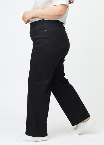 Black high-waisted jeans, which are fitted at the waist and have a loose fit with width down the leg, shown from the side on a plus-size model.