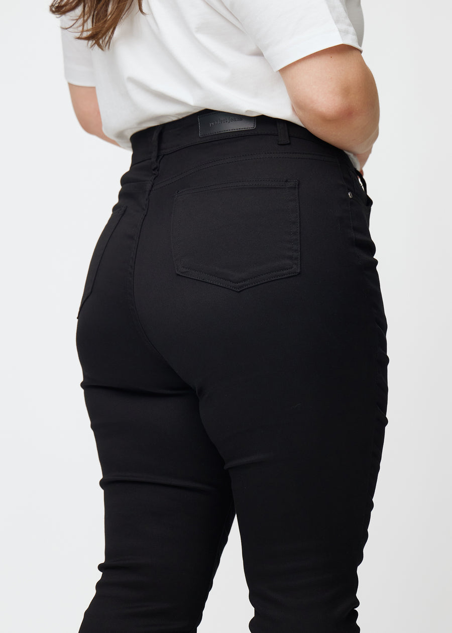 The image shows a close-up of black plus size high rise jeans for women in the color Ravens in skinny fit, seen from the back.