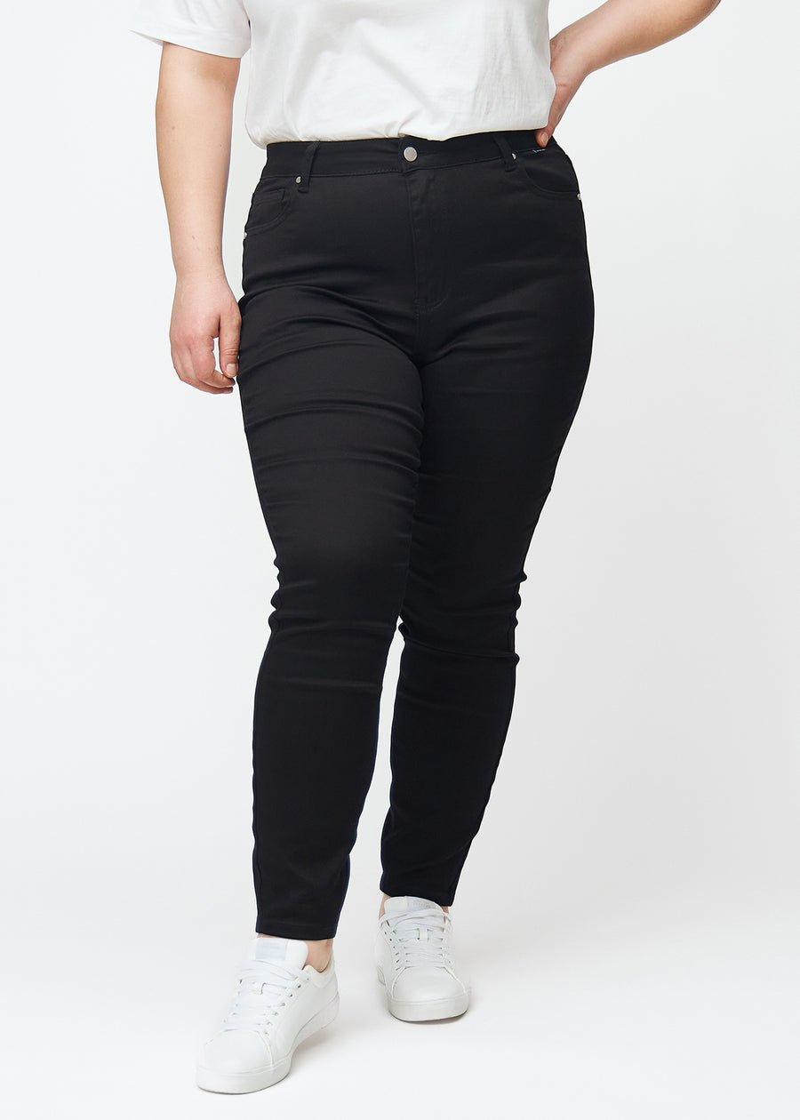 A plus size model showcases black high rise skinny jeans for women in the color Ravens, seen from the front.