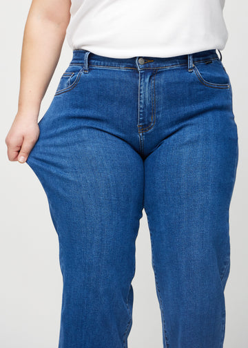 The plus-size model stretches the jeans at the thigh to show the stretch.