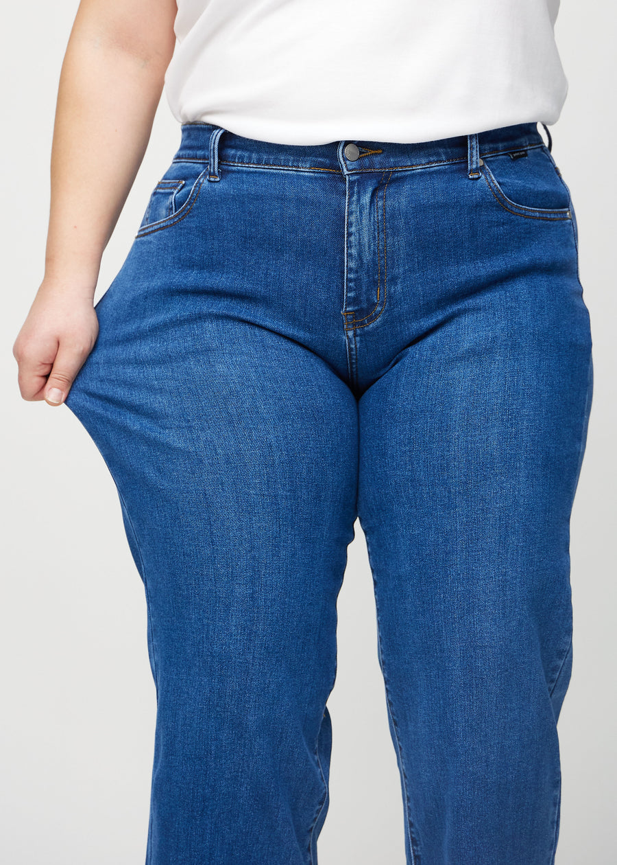 The plus-size model stretches the jeans at the thigh to show the stretch.