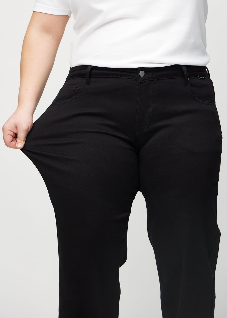 The plus-size model stretches the jeans at the thigh to show the stretch.