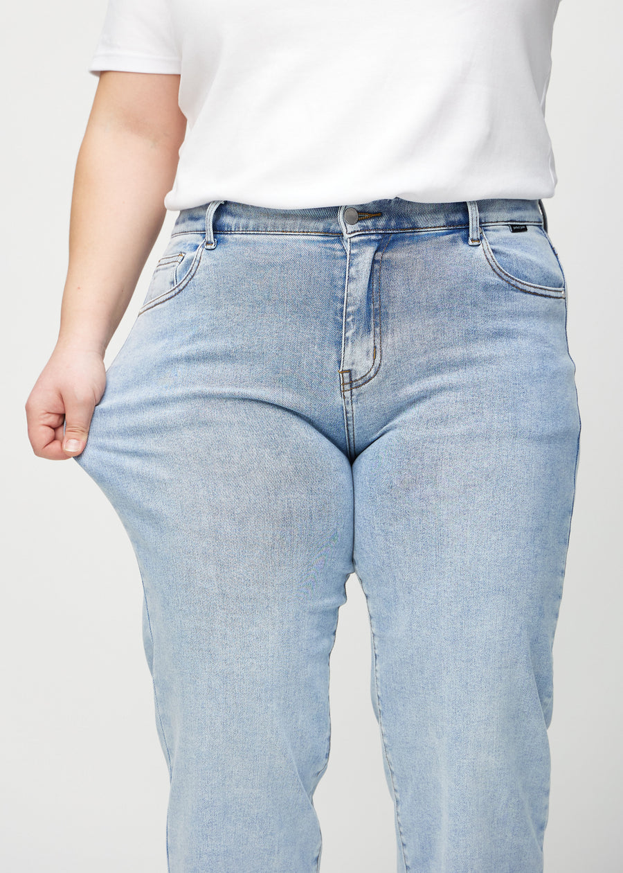 Loose jeans for women in light blue, color Waves. A plus-size model stretches the denim at the thigh to show the fabric&